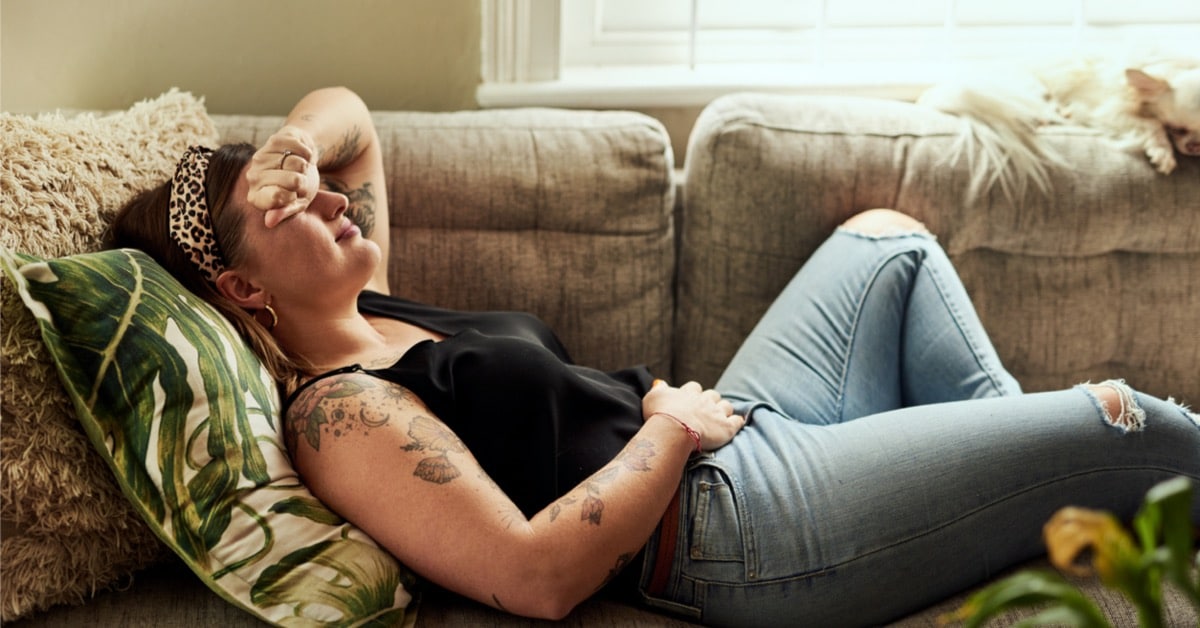 Kvinde med PMS-symptomer, der ligger på sofaen og ømmer sig